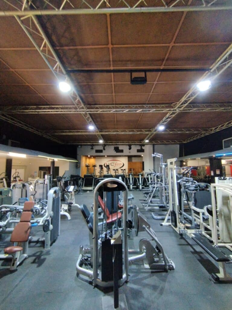 Salle de Sport MC'Form : Musculation et Fitness Salle de sport MC'Form avec équipements Matrix et musculation sous un plafond industriel à éclairage tamisé.