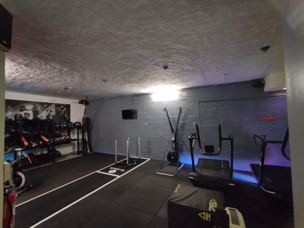 Salle de Musculation Moderne : Équipement Cardio et Sled Salle de gym équipée avec tapis incurvés, rameur et traîneau de musculation Sveltus sur sol noir.